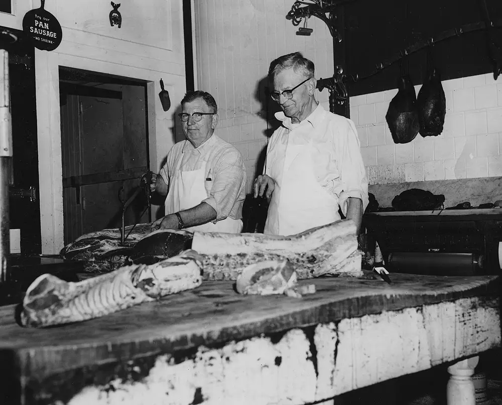 Vintage color photo of two Drier's Meat Market butchers in white aprons preparing meat behind the counter