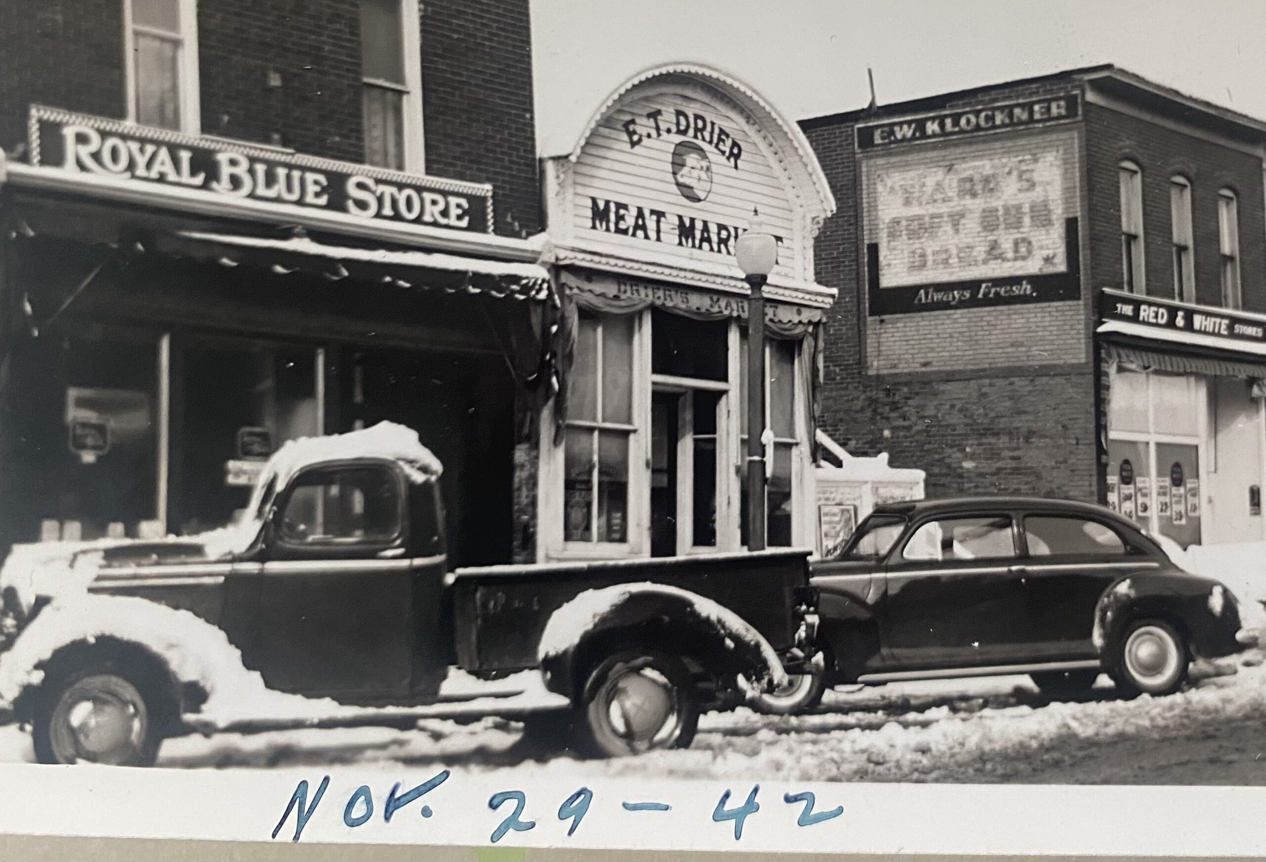 Historic 1942 photo of the original E.T. Drier Meat Market storefront in Three Oaks, Michigan, next to the Royal Blue Store, with vintage vehicles parked in the snow